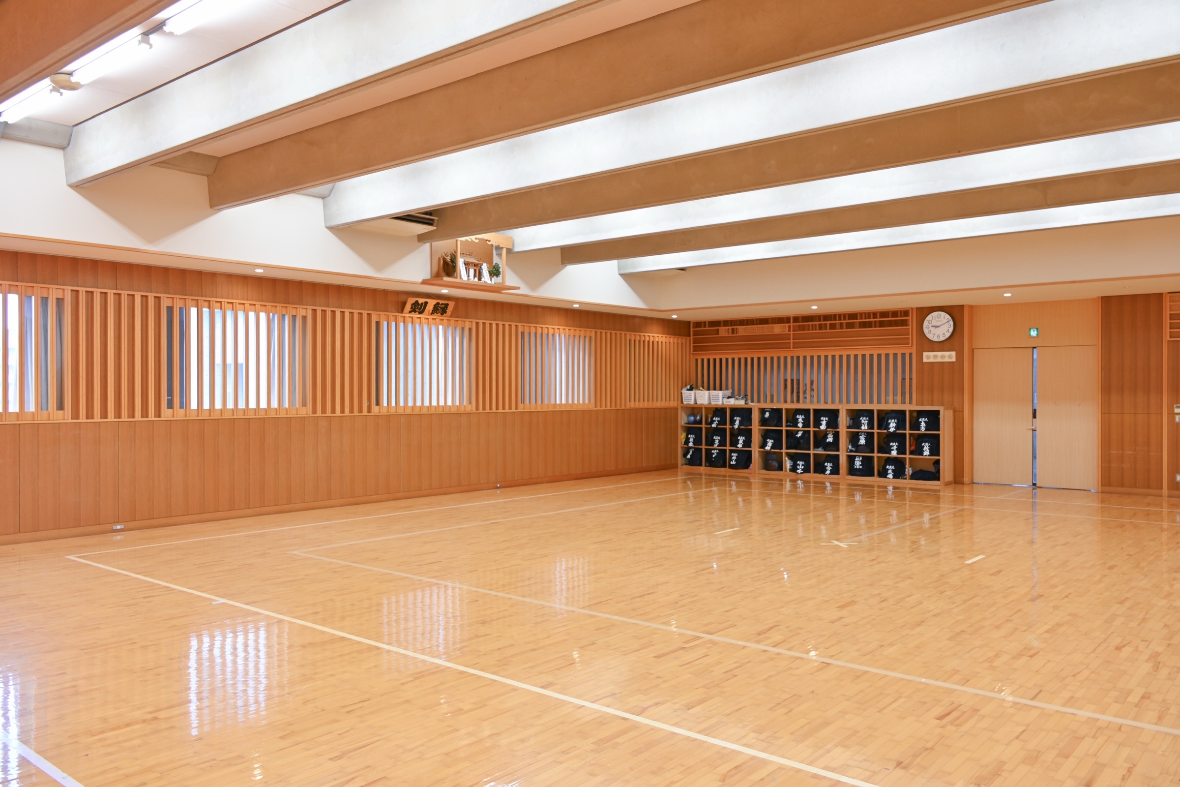武蔵大学10号館5階の武道場内観。『剣縁』の扁額と木目の壁、整然と並ぶ防具袋、磨かれた木床の道場。